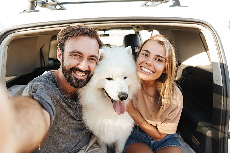 Blog - Portrait of a Cheerful Couple Sitting in the Back Trunk of Their Car with Their Dog in Between Them